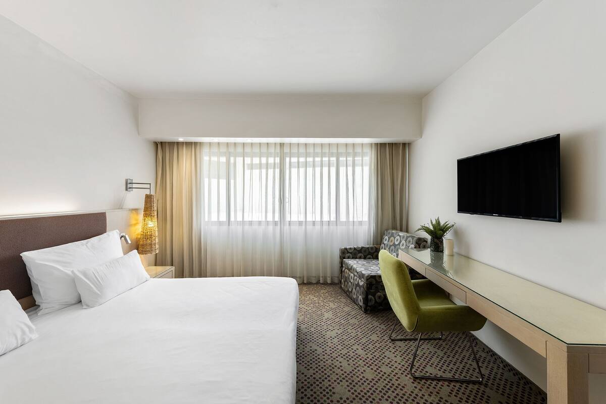 A hotel room with a bed, a desk, a chair, a television, and a window with curtains.
