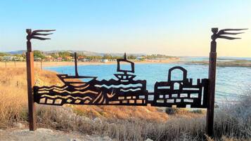 A metal gate with a wave pattern and a boat silhouette, set against a coastal backdrop with a clear sky.