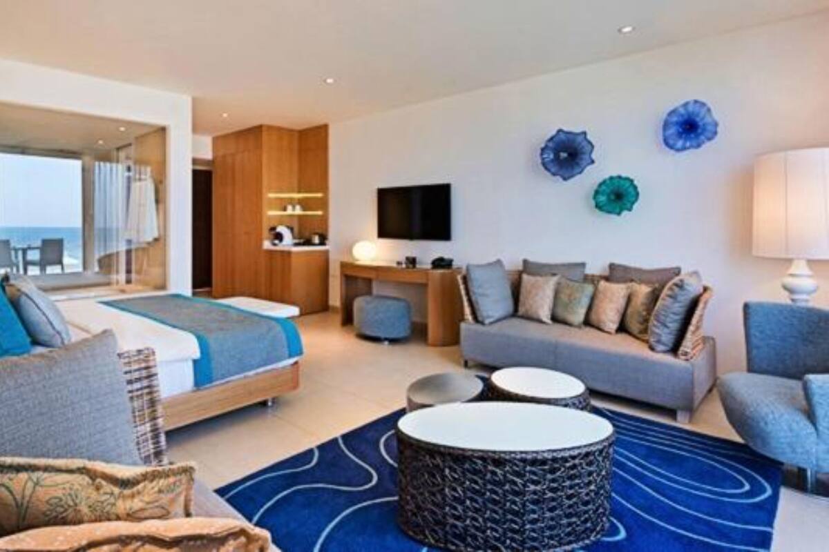 A modern hotel room with a bed, sofa, and armchair, a desk, and a TV.