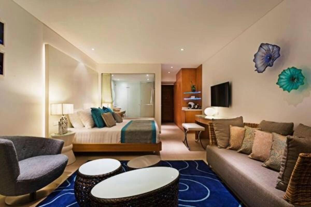 A modern hotel room with a bed, a sofa, a chair, a small table, and decorative wall art.