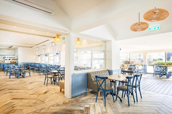 A spacious restaurant with high ceilings, wooden flooring, and blue chairs.