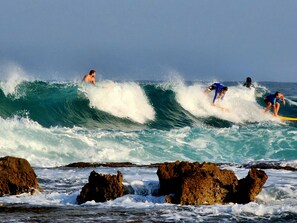 A beach with surfers riding waves and rocky outcrops in the foreground. - Nachsholim Holiday Village Hotel (Hof HaCarmel)