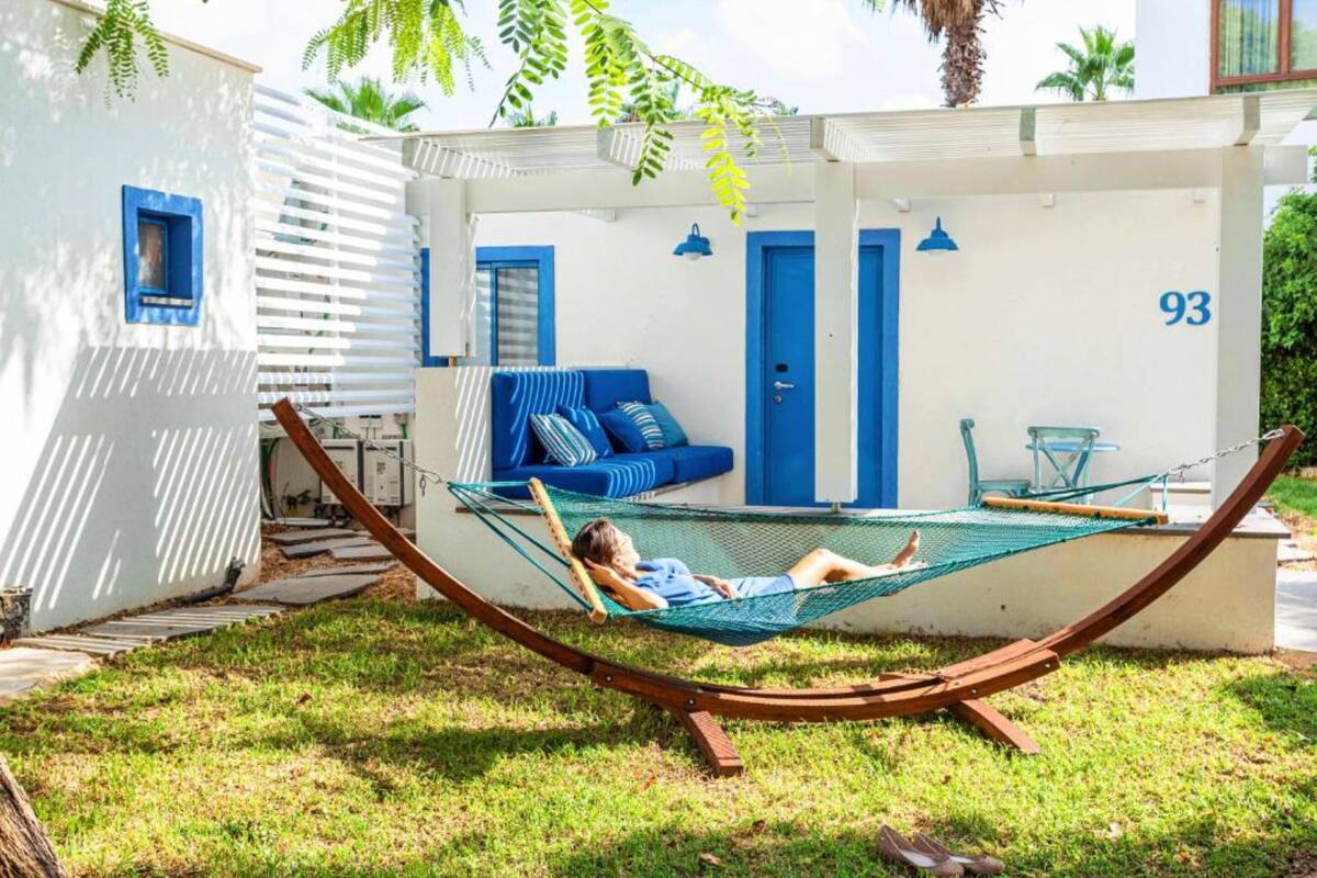 A person relaxing in a hammock on a lawn in front of a building with a blue door and number 93.
