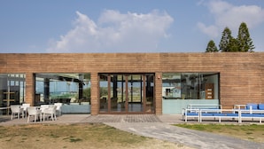 Un edificio moderno con grandes puertas de cristal, asientos exteriores y vistas del paisaje circundante.