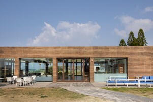 Un edificio moderno con grandes puertas de cristal, asientos exteriores y vistas del paisaje circundante.