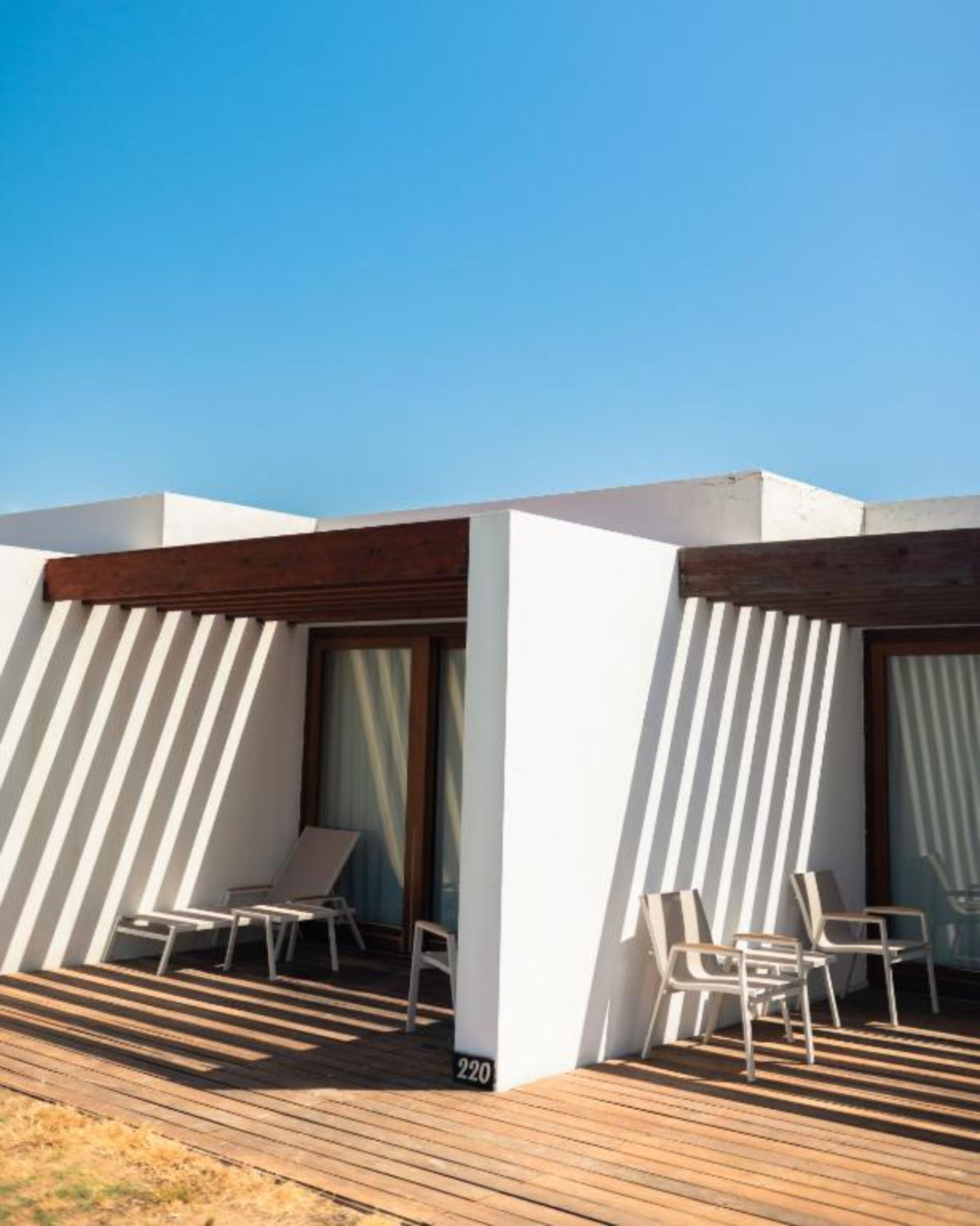 Un espacio al aire libre moderno con paredes blancas y listones de madera, que incluye dos sillones de relax y una mesa.