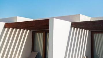 Un espacio al aire libre moderno con paredes blancas y listones de madera, que incluye dos sillones de relax y una mesa.