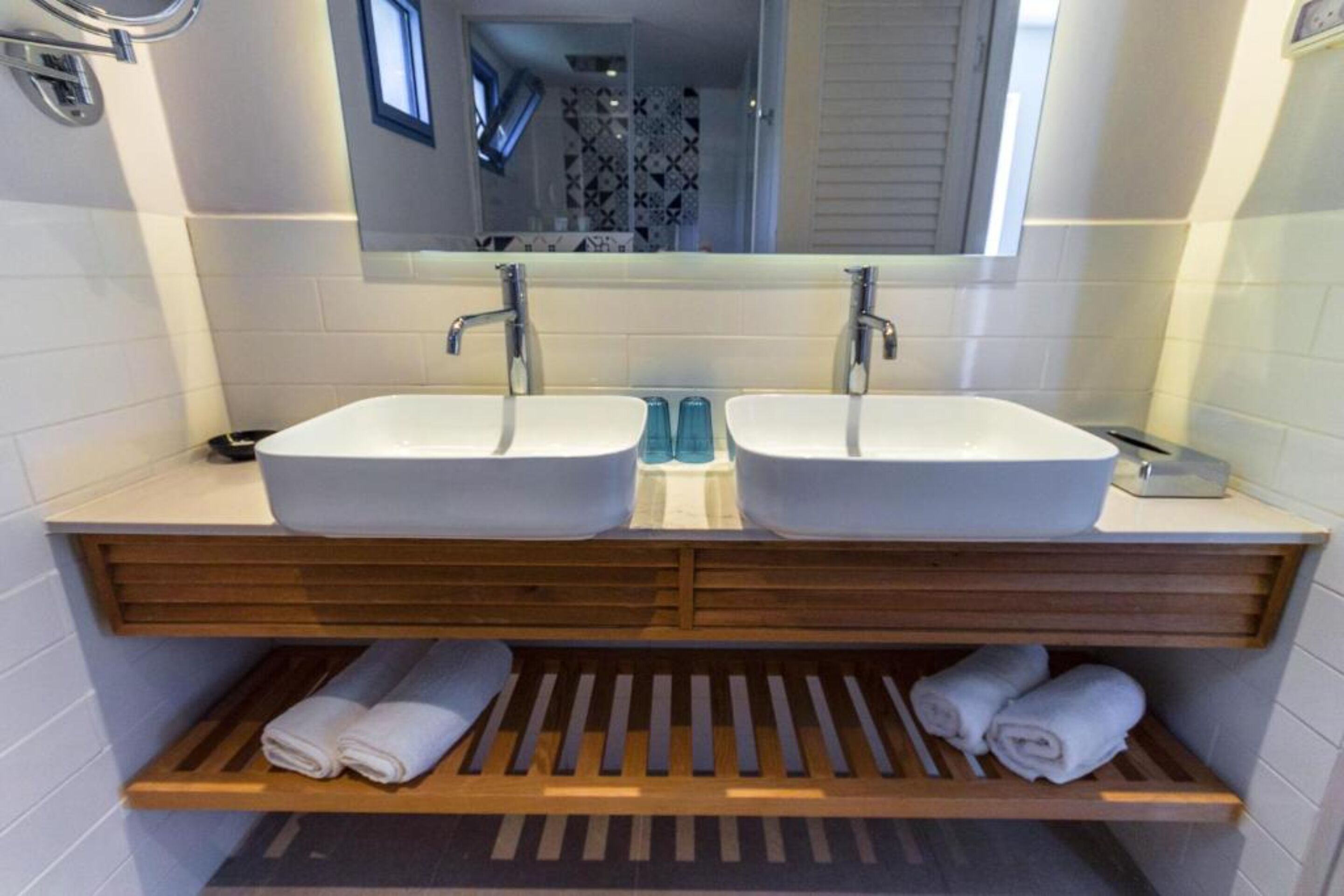 Une salle de bain avec deux lavabos, un miroir et des étagères en bois où sont posées des serviettes.