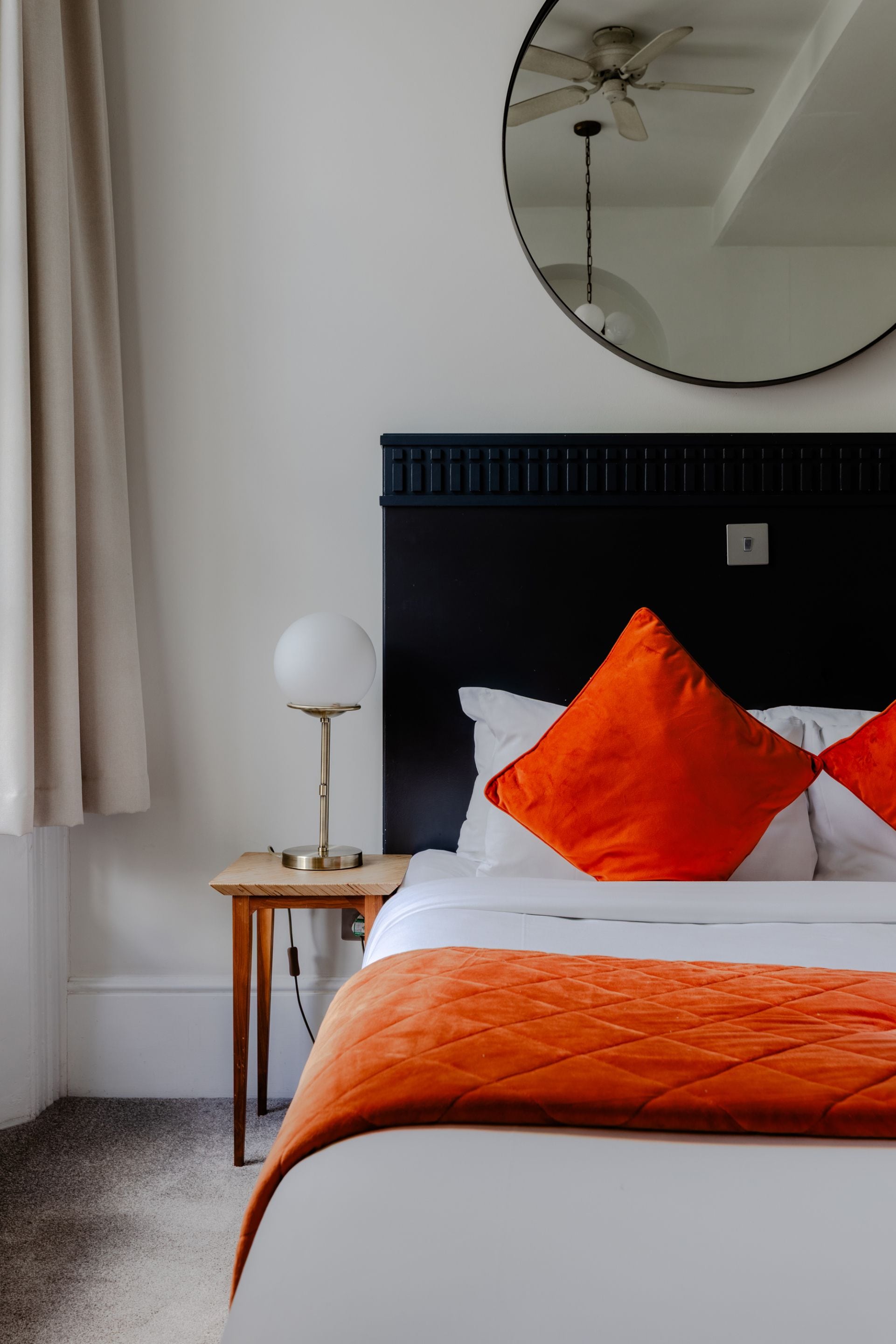 Ein Hotelzimmer mit Bett, rundem Spiegel, Deckenventilator und Nachttisch mit Lampe.