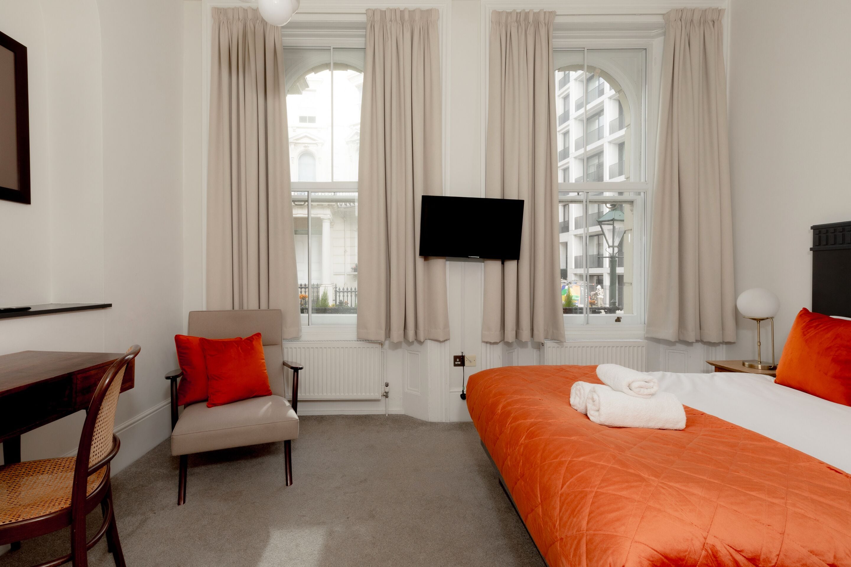Ein Hotelzimmer mit Bett, Sessel, Schreibtisch und Fernseher.