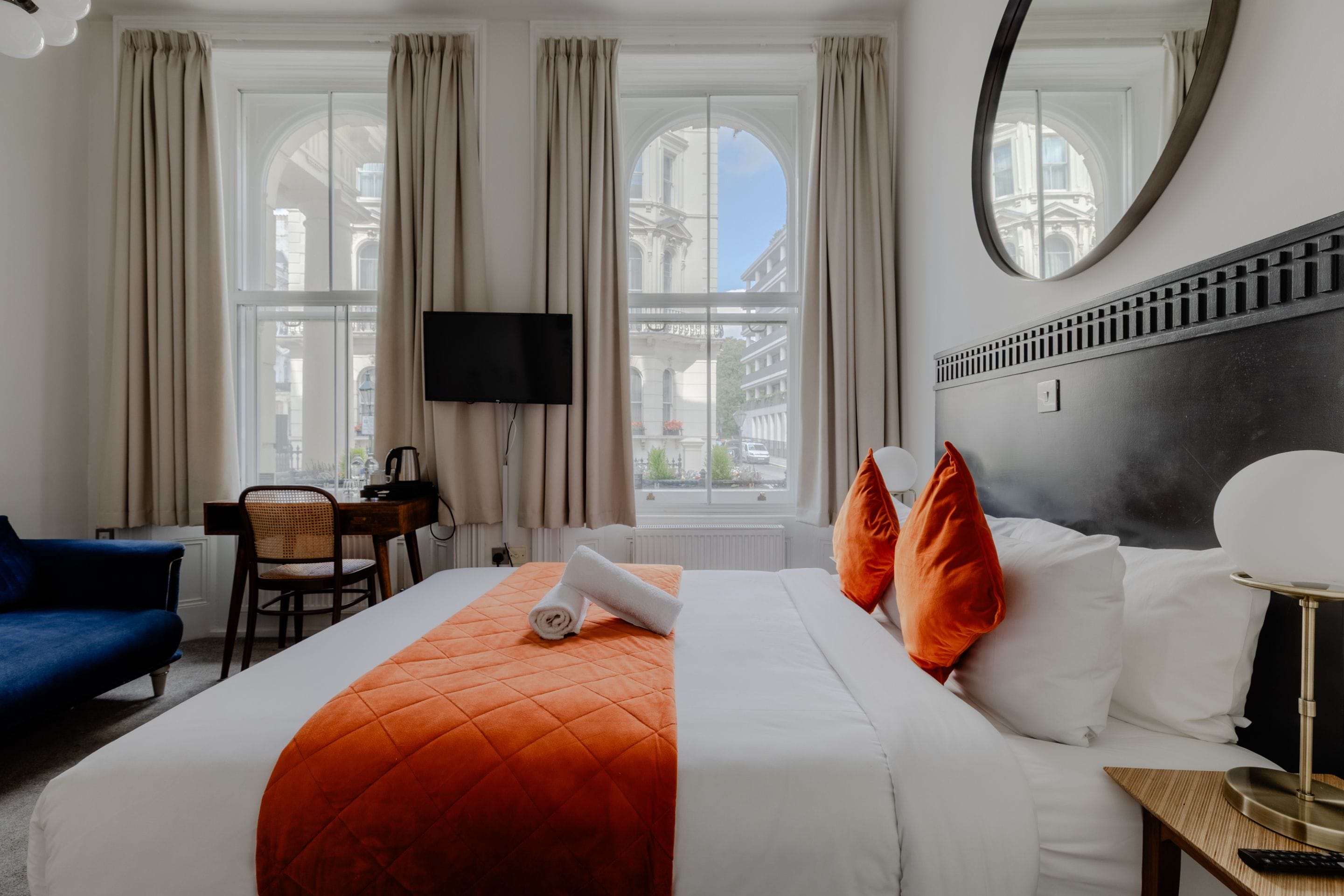 A hotel room with a bed, a desk, a chair, a TV, and a view of the city.