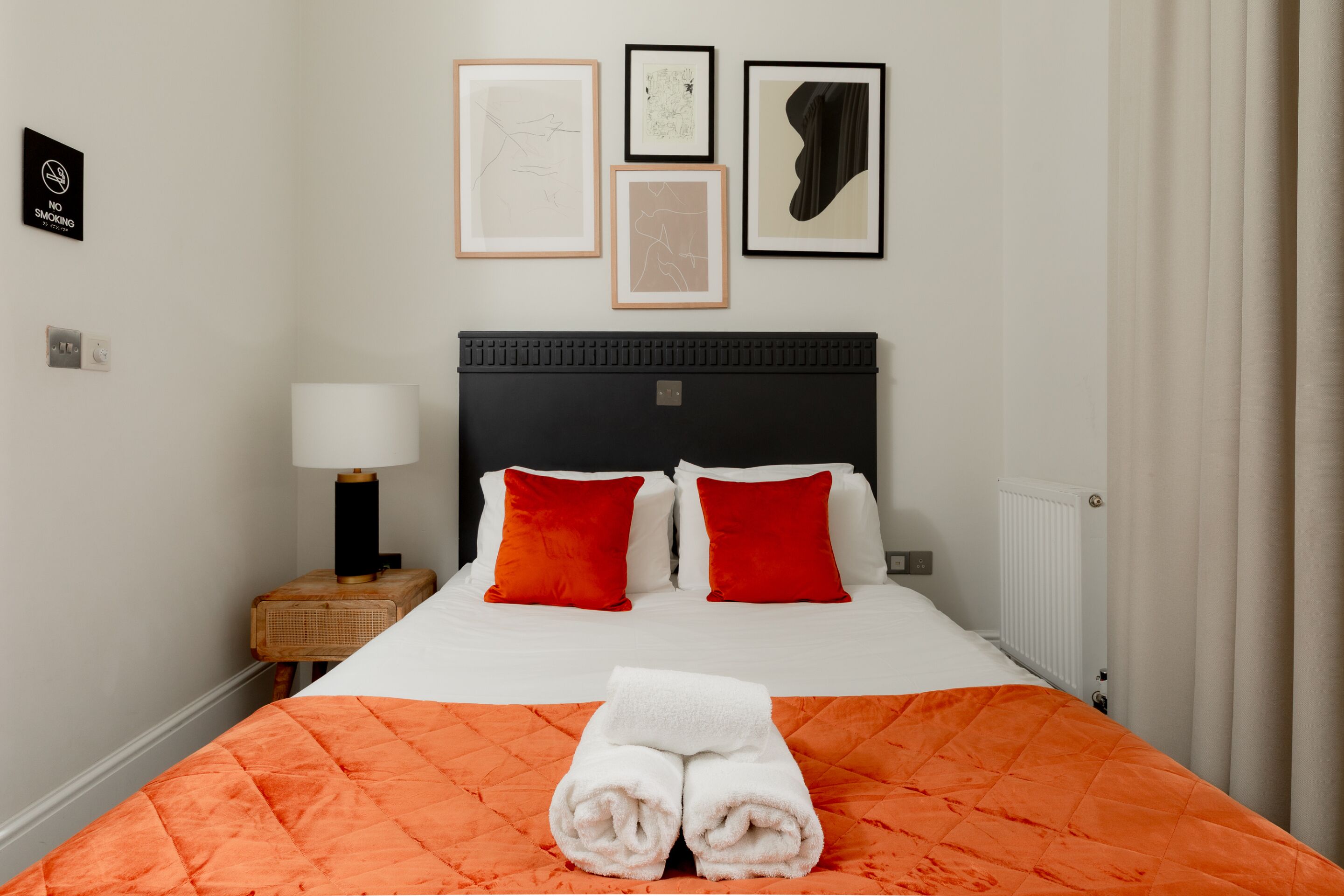 Una habitación de hotel con cama, mesita de noche, lámpara y cuadros en la pared.