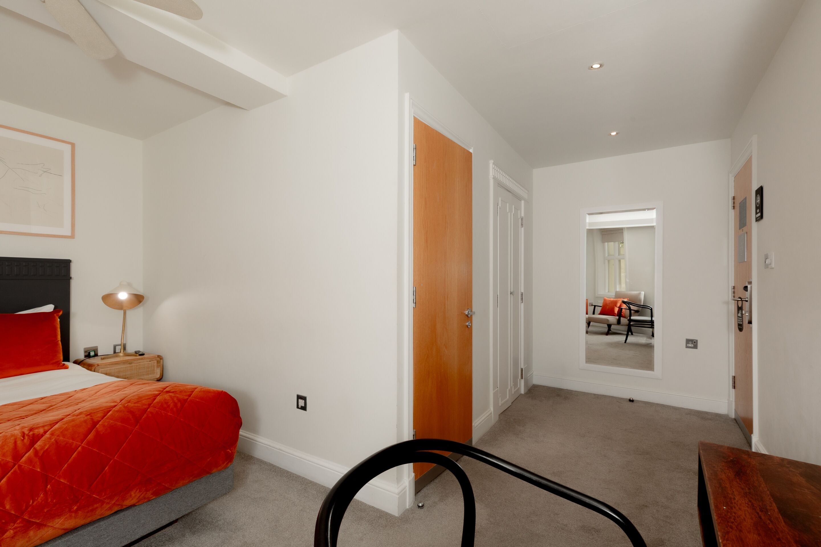 A bedroom with a bed, a nightstand, a lamp, and a wooden door.