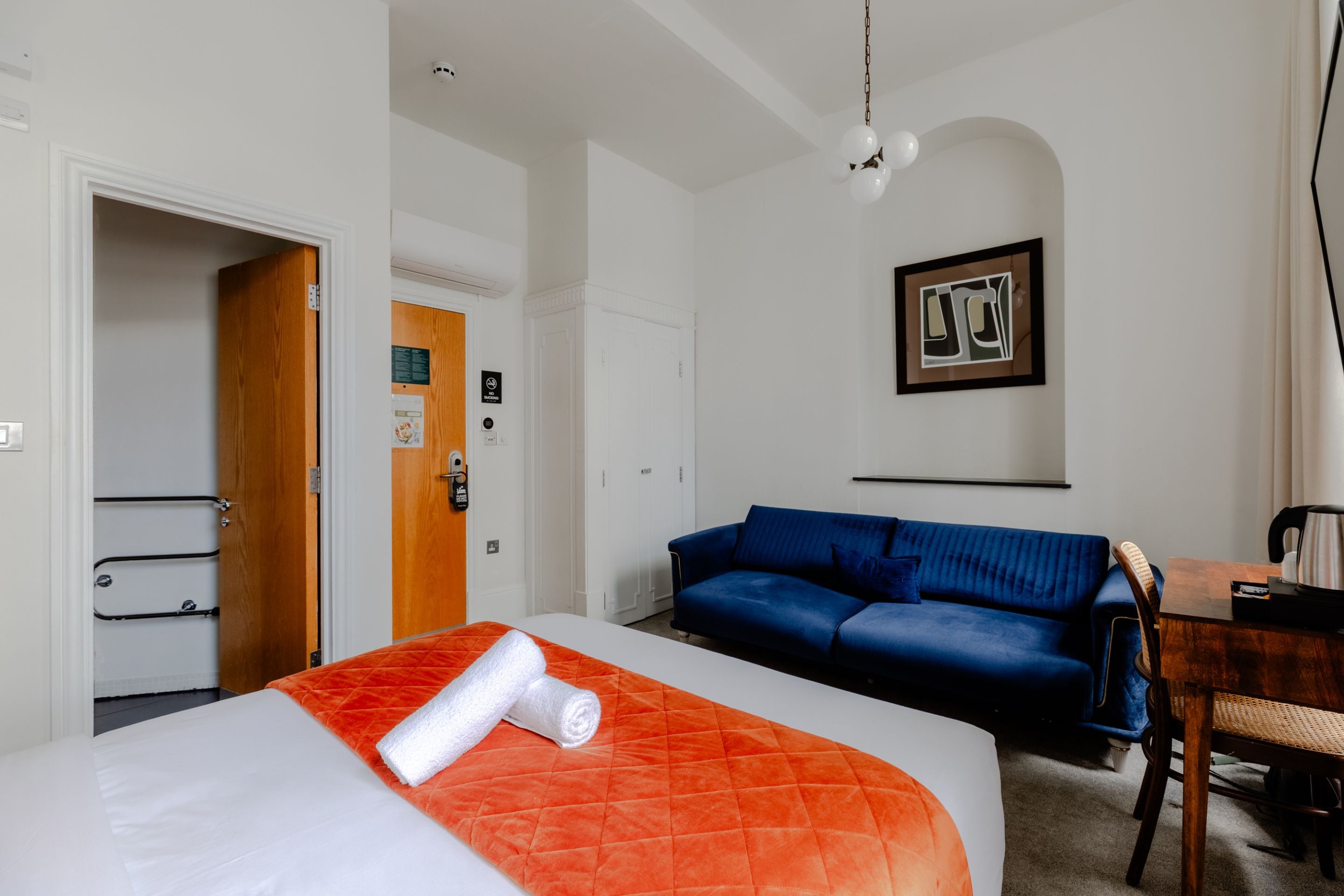 Ein Hotelzimmer mit einem Bett, einem blauen Sofa, einer Holztür und einem gerahmten Bild an der Wand.