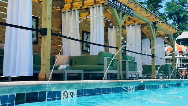 A poolside area with a wooden pergola, green seating, and a sign reading "LE JARDIN BLEU". - Uncommoner Hotel by Reverie Boutique Collection (West Yarmouth)