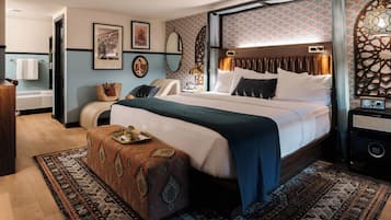 A bedroom with a large bed, a bedside table with a radio, a wall-mounted mirror, and a patterned rug.