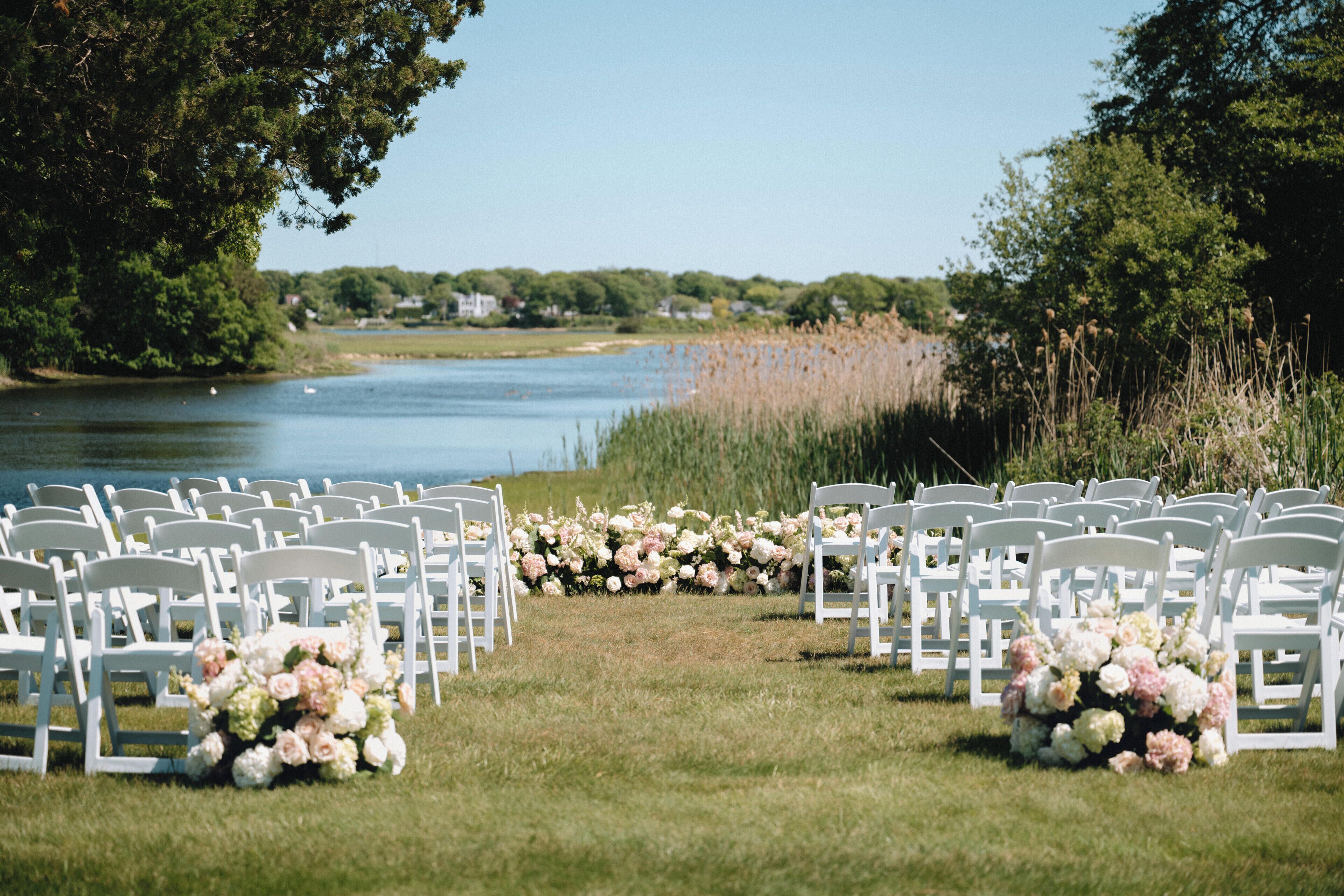 A riverside wedding ceremony setup with white chairs and floral arrangements.