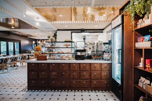 A cafe interior with a central counter, storage drawers, and a refrigerator stocked with beverages. - Uncommoner Hotel by Reverie Boutique Collection (West Yarmouth)