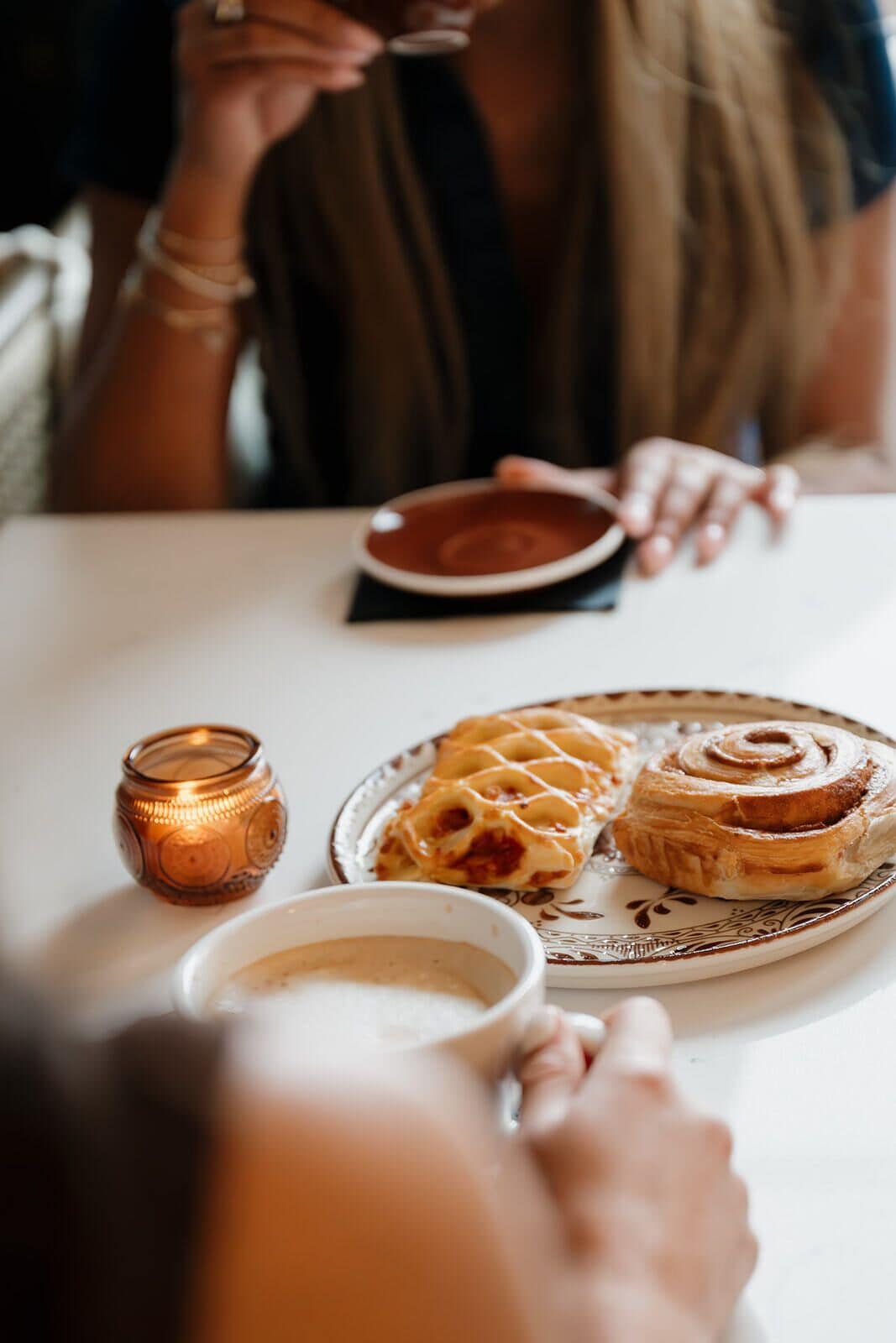 A dining table with a plate of food, a cup, and a candle.