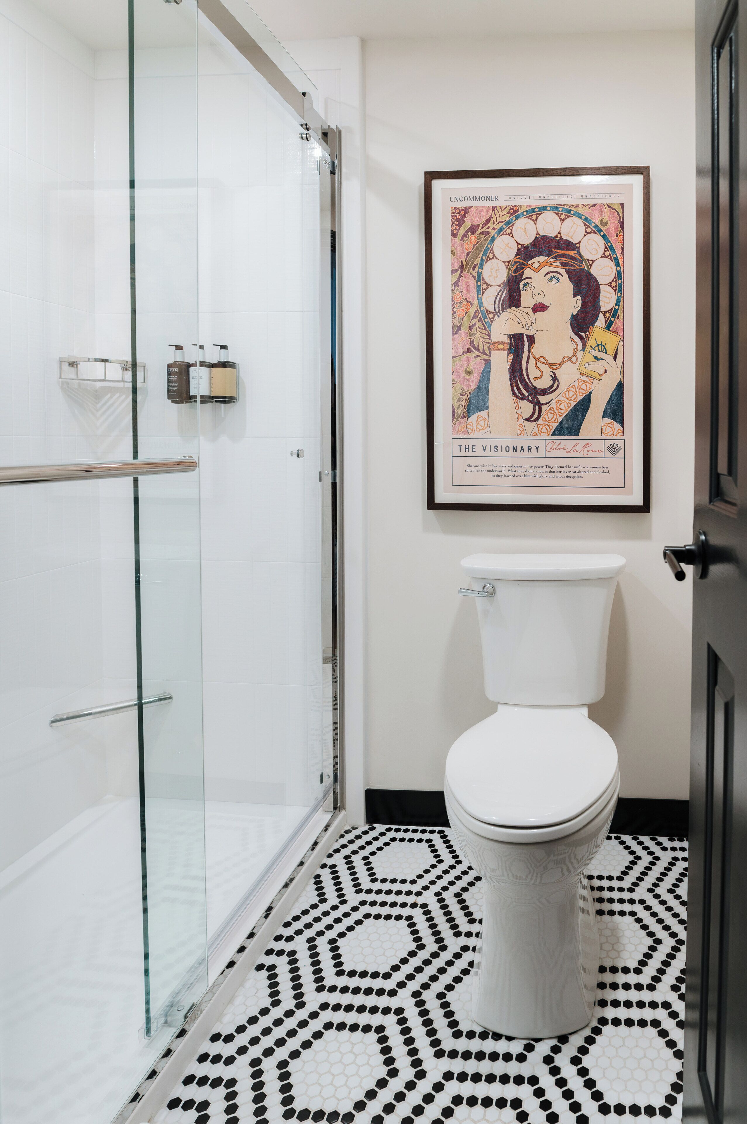 Un baño con cabina de ducha de vidrio, un inodoro blanco y un suelo con estampado blanco y negro.