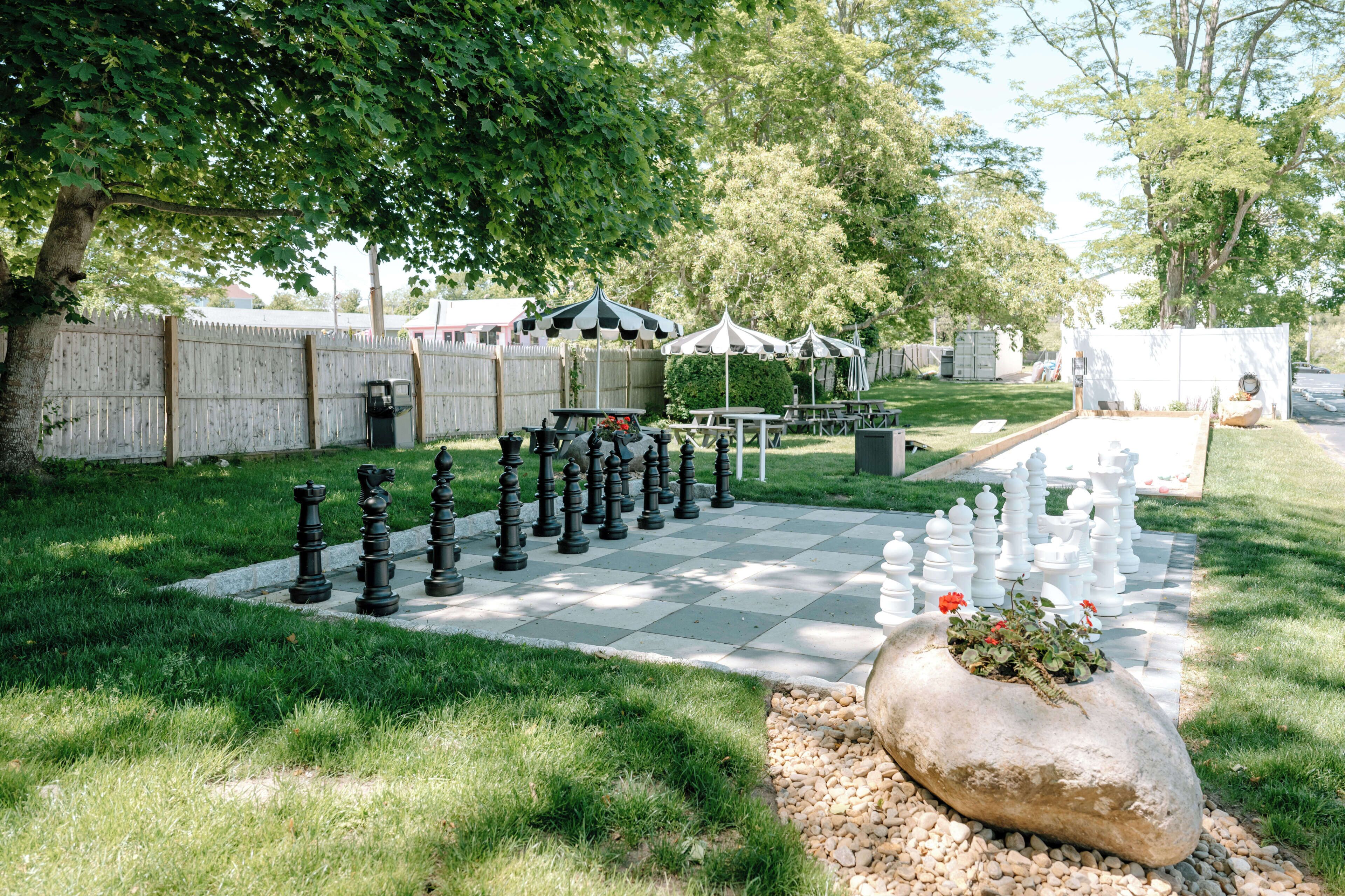 A chessboard set up outdoors with tables and umbrellas in the background.