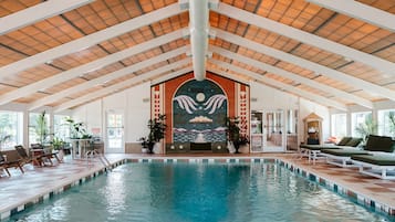 An indoor swimming pool with a high ceiling, lounge chairs, and potted plants.