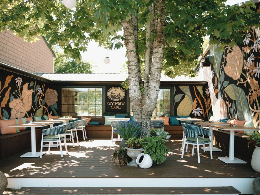 Un área de estar al aire libre con mesas y sillas, rodeada de muros decorativos y plantas.
