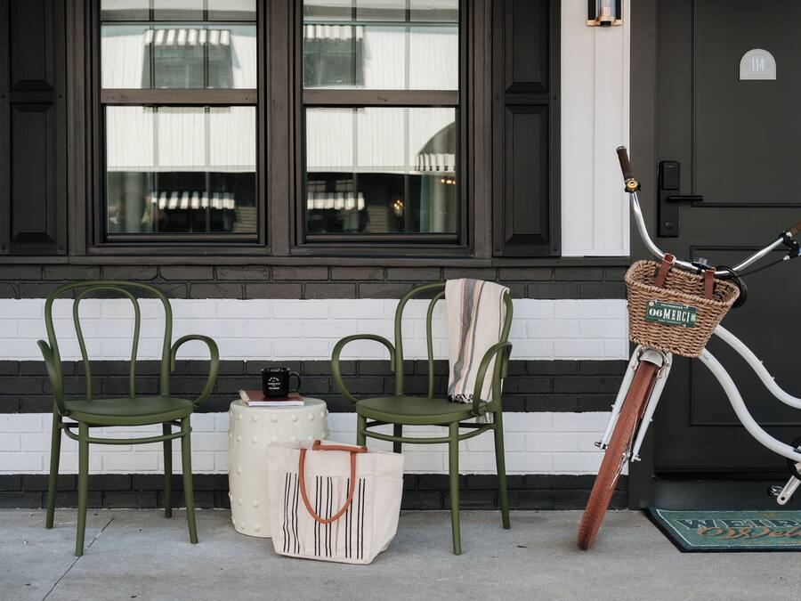Two green chairs, a white table with a black mug, a white tote bag, and a wicker bike basket with a handle.