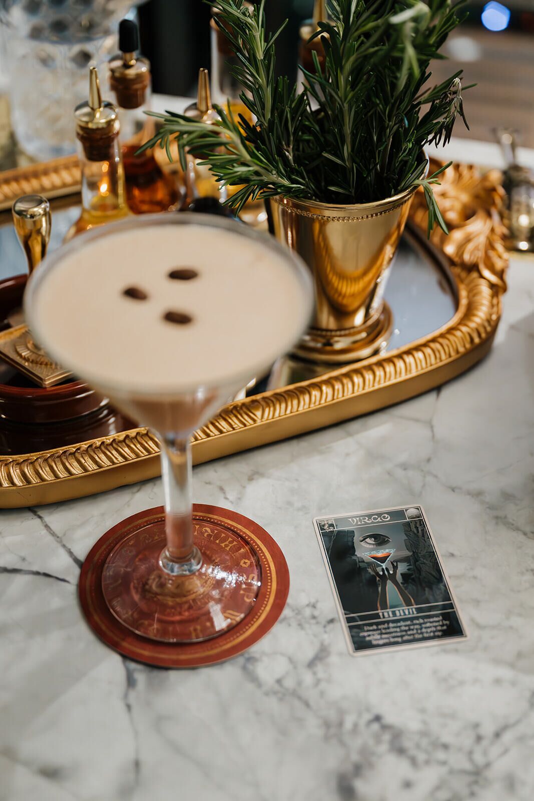 Una copa de martini sobre una mesa de mármol con una bandeja dorada y una tarjeta.