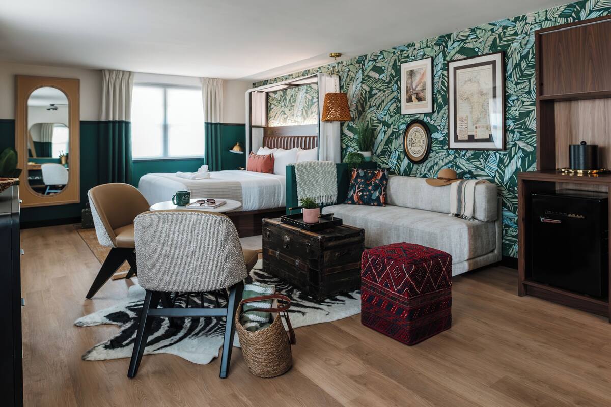 Una habitación de hotel acogedora con cama, sofá, sillón, mesita y cómoda.
