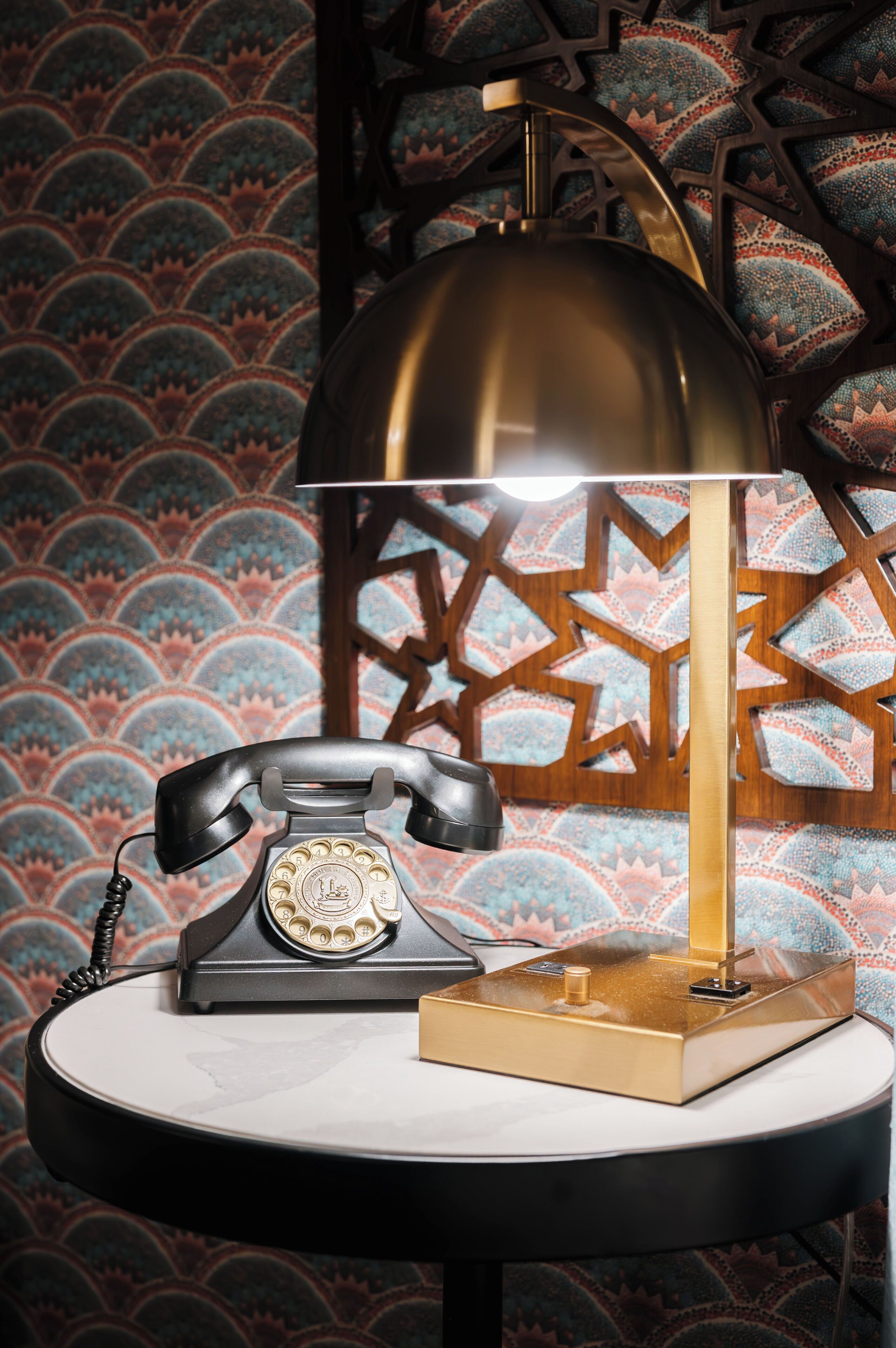 Un vieux téléphone à cadran sur une table ronde, avec une lampe dorée et un livre.