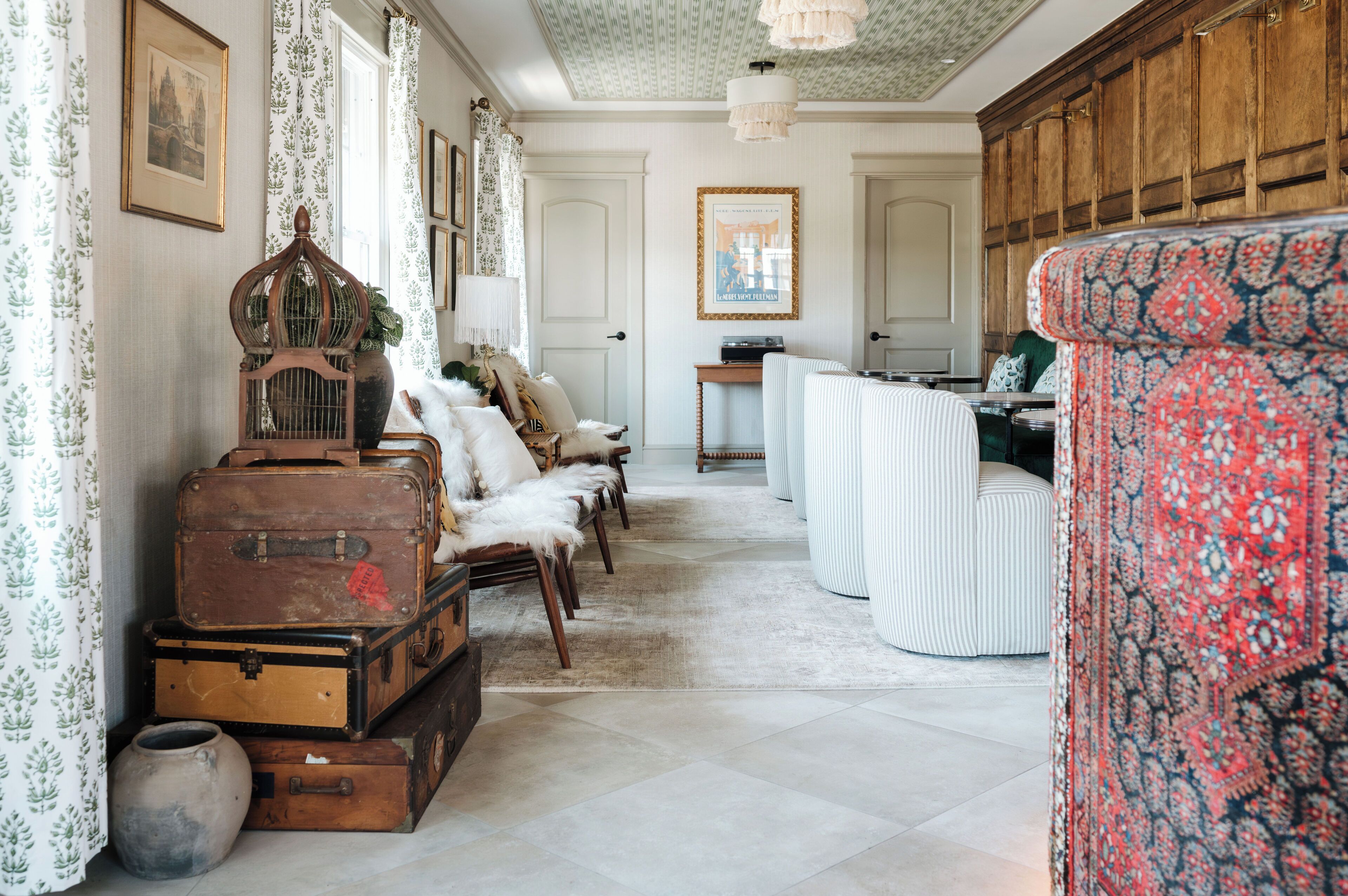Une pièce avec un tapis à motifs, des valises anciennes, une cage à oiseaux en bois et un fauteuil à motifs.