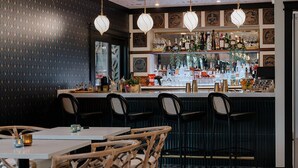 A bar area with a patterned wall, wicker chairs, and a tiled floor. - Uncommoner Hotel by Reverie Boutique Collection (West Yarmouth)