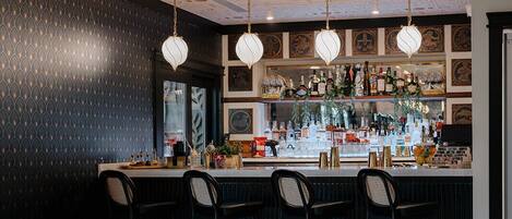 A bar area with a patterned wall, wicker chairs, and a tiled floor.