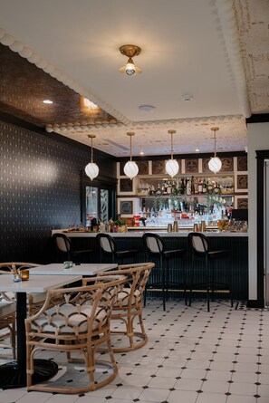 Un área de bar con pared estampada, sillas de mimbre y suelo de baldosas.