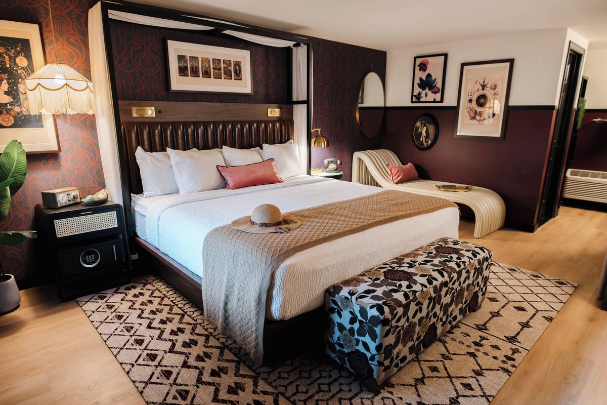 Un dormitorio bien amoblado con una cama grande, una mesita de noche con lámpara, un banco decorativo y un espejo en la pared.