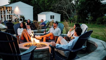 A group of people seated around a fire pit in an outdoor setting with a house in the background.