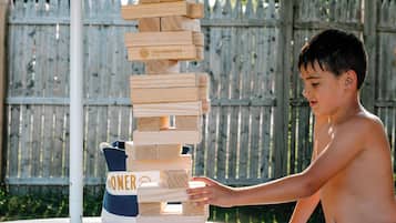 A child playing with wooden blocks on a table outdoors, with a wooden fence and a tent in the background.