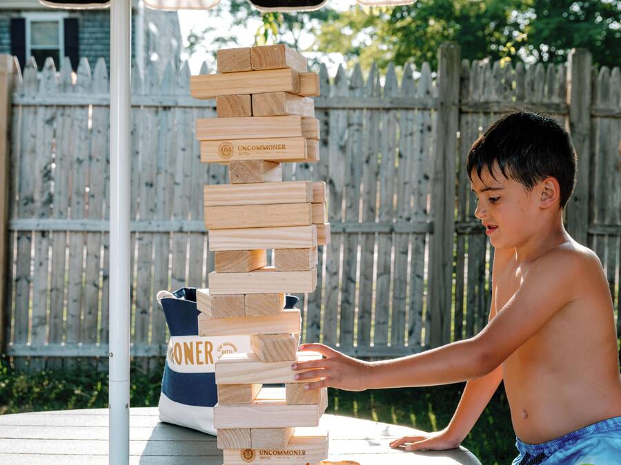 A child playing with wooden blocks on a table outdoors, with a wooden fence and a tent in the background.