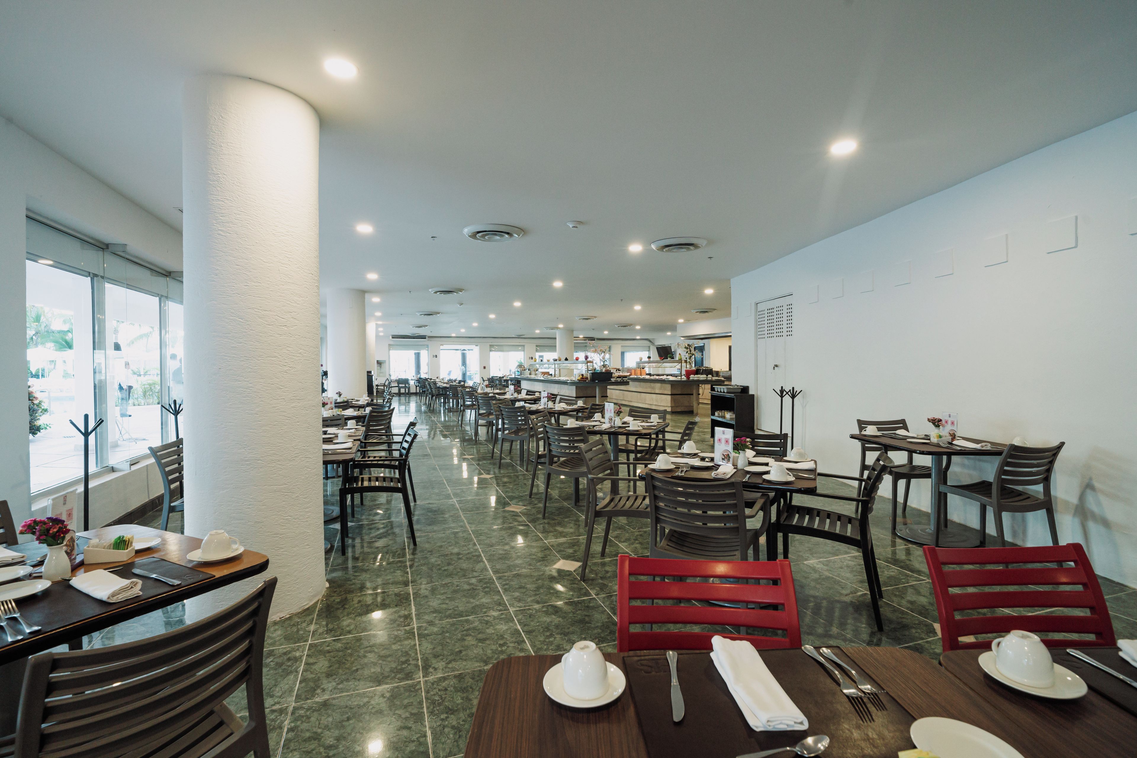 Un restaurante espacioso con varias mesas y sillas, un pilar grande y vistas a través de las ventanas.