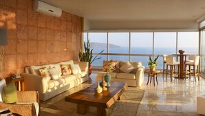 Un amplio salón con un gran ventanal con vistas al mar, una zona de estar acogedora con un sofá y sillones, y una pequeña mesa redonda.