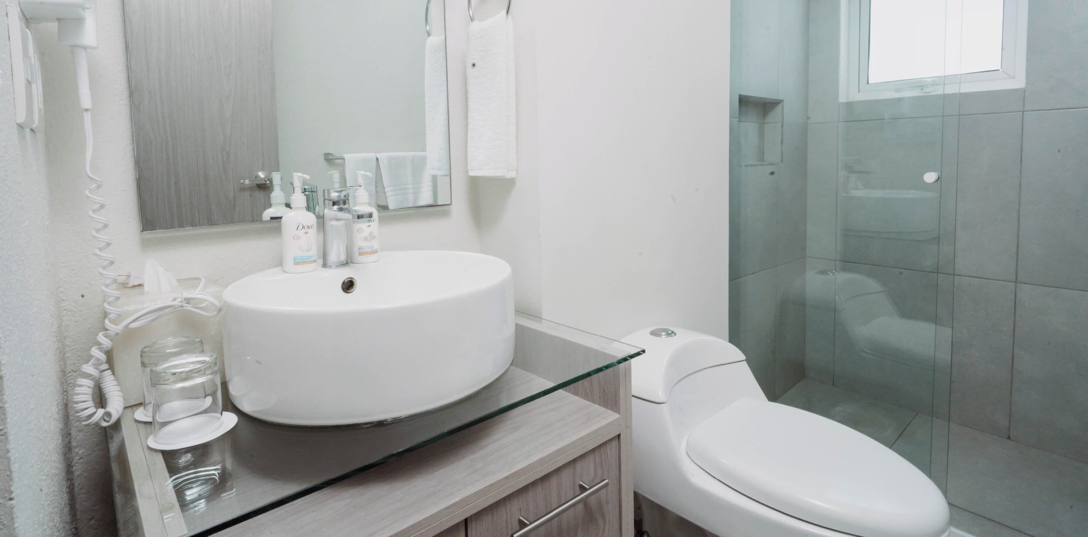 Un baño moderno con un lavabo con tapa de vidrio, un inodoro y una ducha con cerramiento de vidrio.