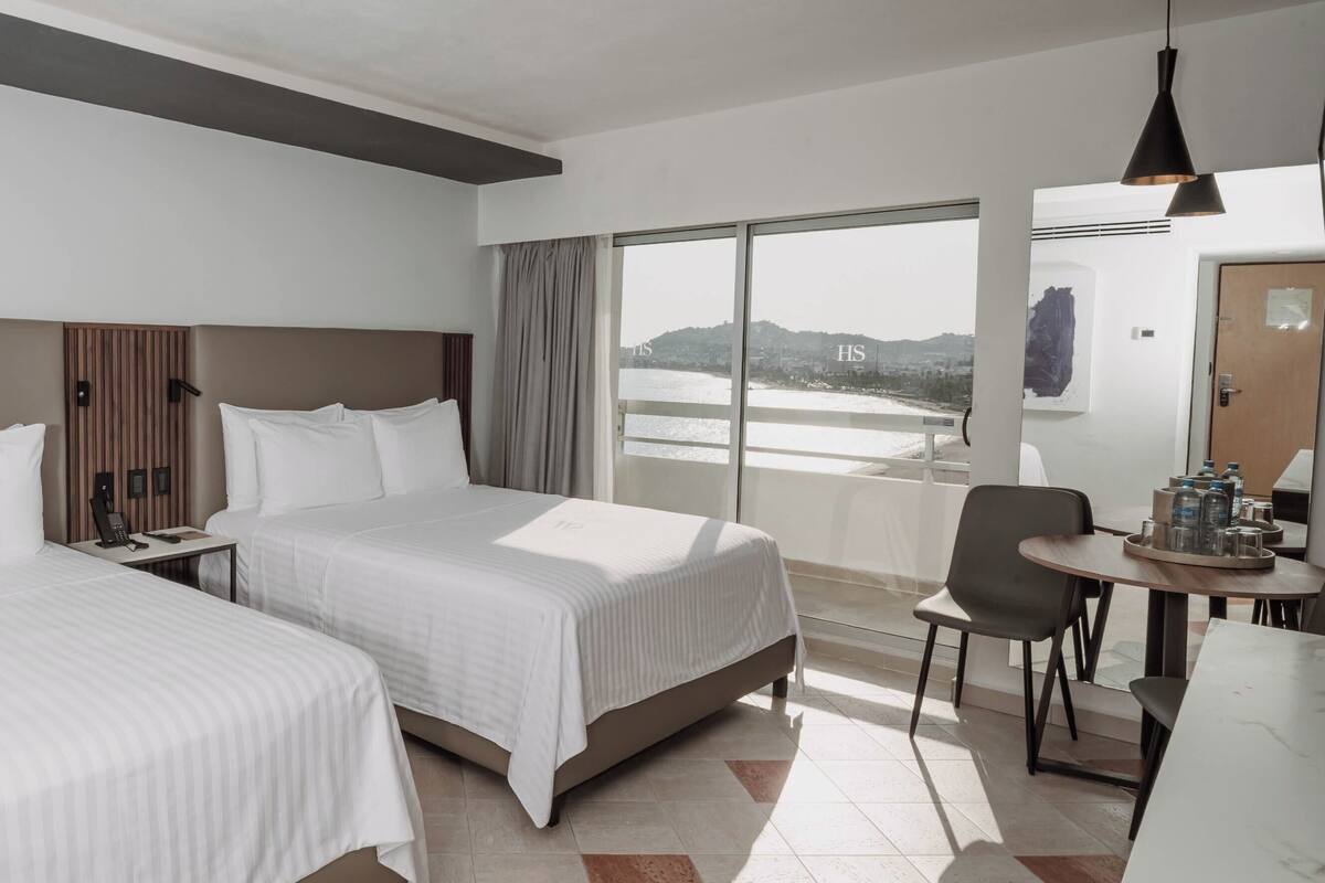 A hotel room with two beds, a desk, a chair, and a view of a body of water.