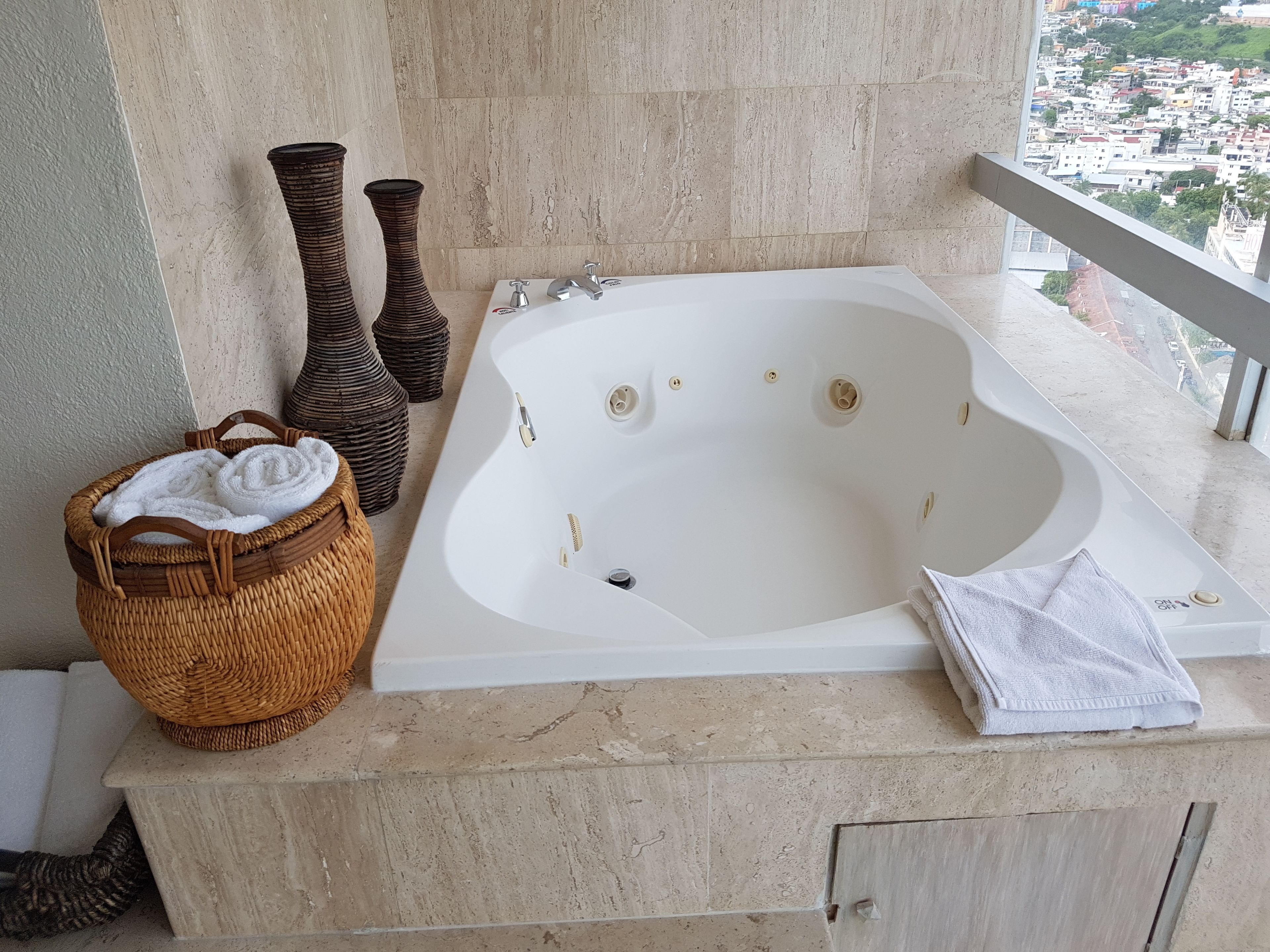 Un baño con una bañera independiente, una cesta de mimbre con toallas y dos jarrones sobre una encimera de mármol.