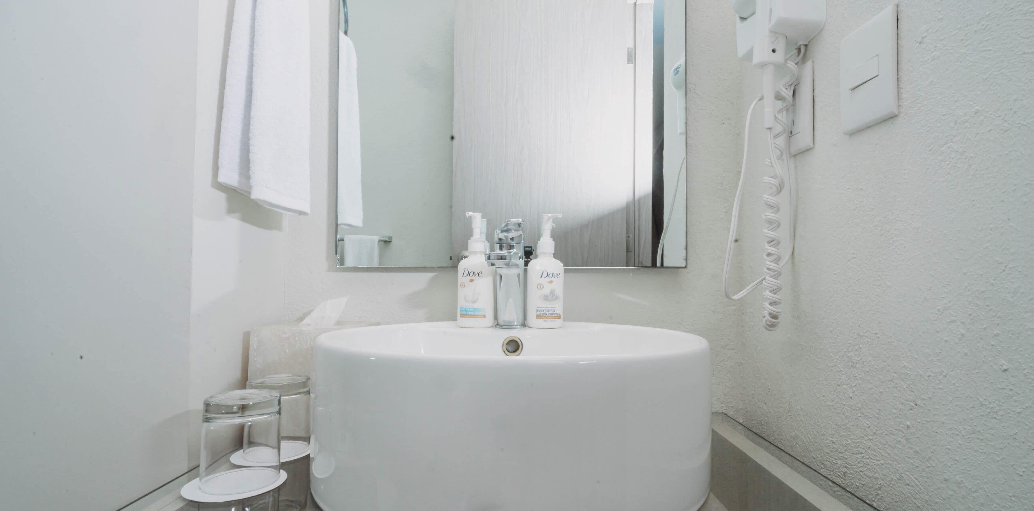 A bathroom with a white sink, two Dove hand soap bottles, a glass soap dispenser, and a white telephone mounted on the wall.