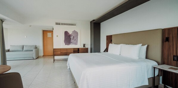 A modern hotel room with a large bed, a desk, a sofa, and a wall-mounted artwork. - HS HOTSSON Hotel Acapulco (Acapulco)