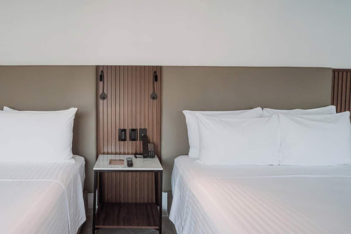 A hotel room with two beds, a small table with a phone and a lamp, and a wooden panel wall.