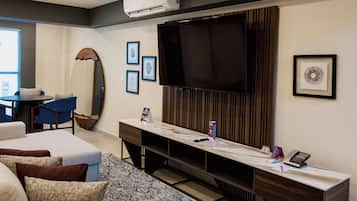 A modern hotel room with a sofa, a desk with a flat-screen TV, a large mirror, and framed pictures on the wall.