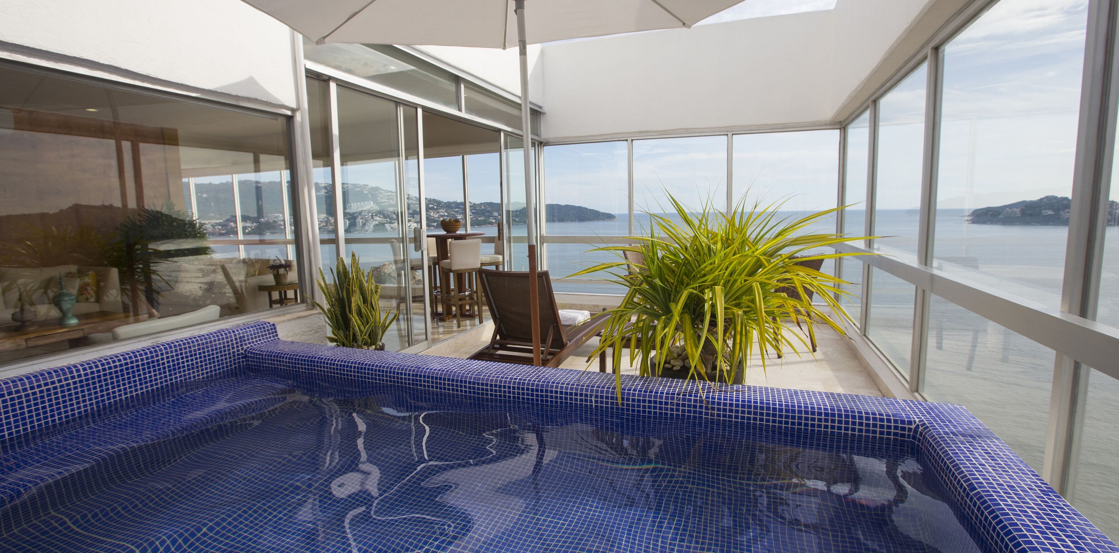 Una piscina interna moderna con vista sul mare e un'area balcone con sedute e piante.