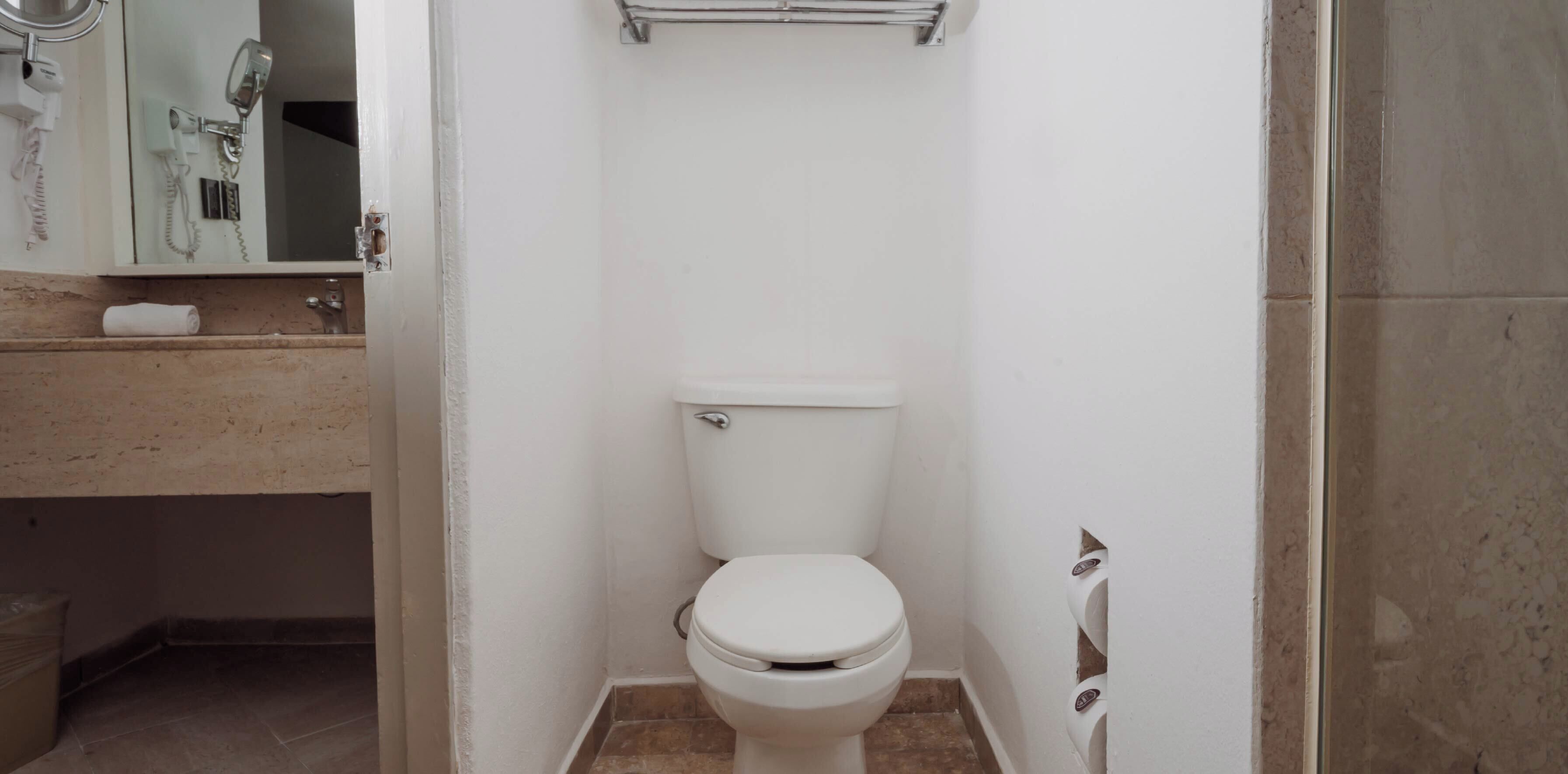 A small, white bathroom with a toilet, a towel dispenser, and a mirror.